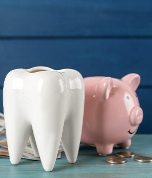 A large ceramic tooth model next to a piggy bank and some dollar bills