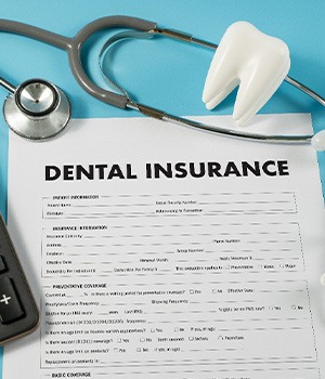 A dental insurance form next to a calculator and some dental tools