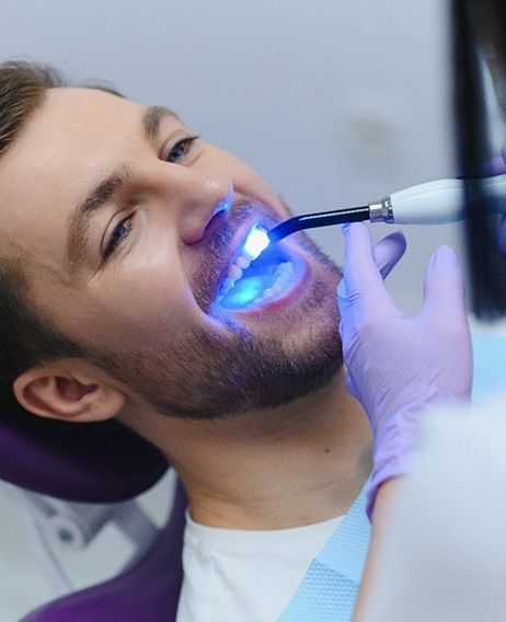 Dentist applying UV light to man’s dental bonding