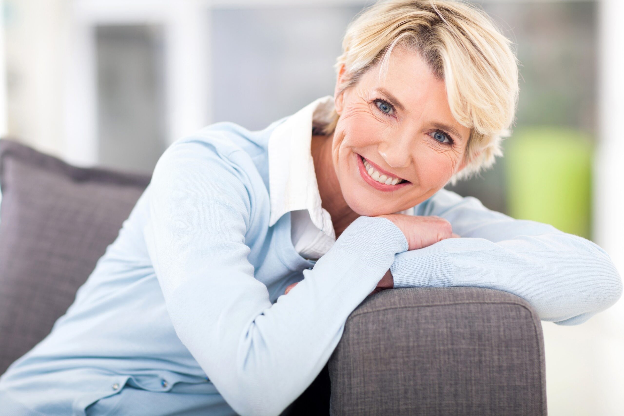 Smiling older woman resting on couch arm.