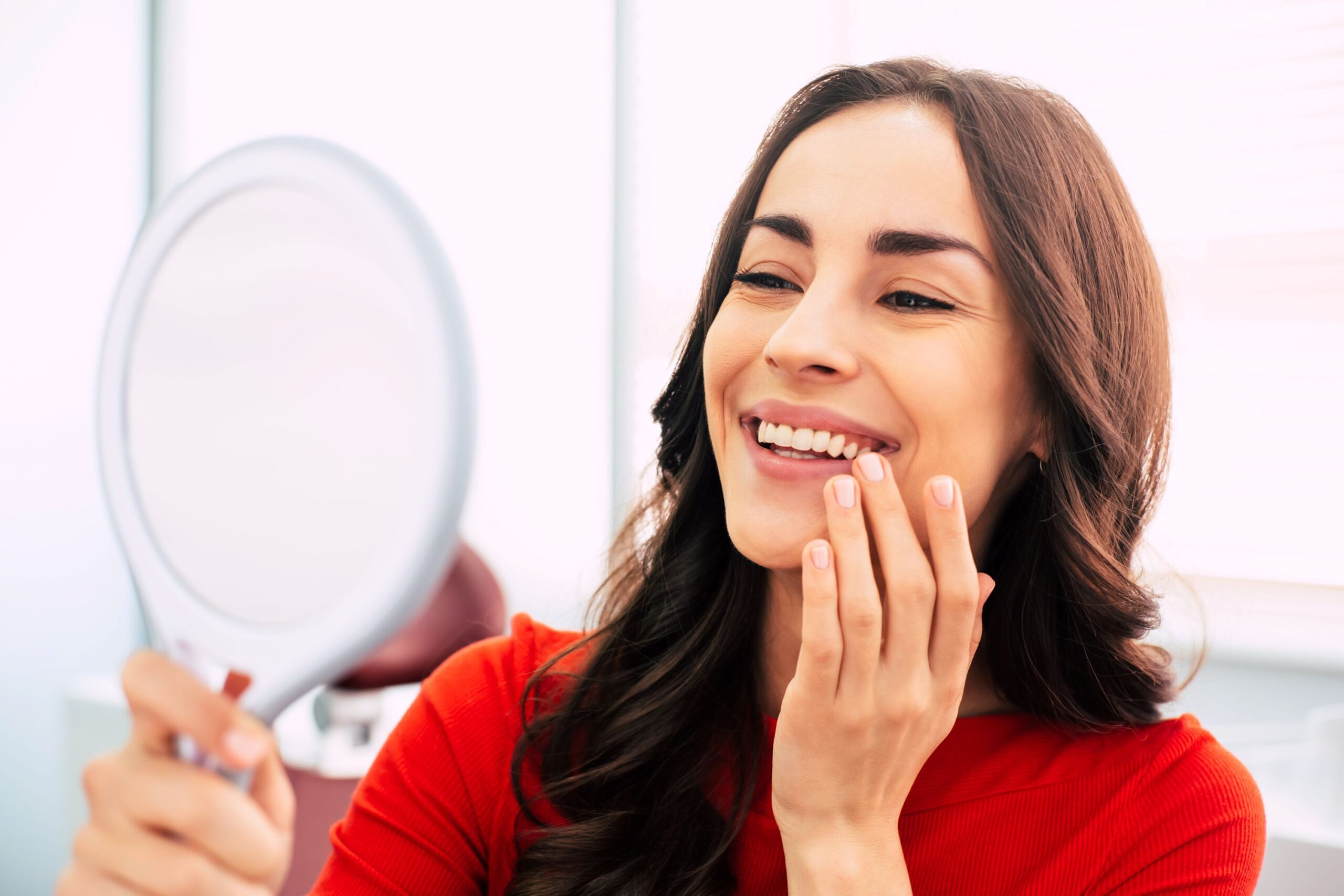 Woman in red-orange shirt smiling at her reflection.