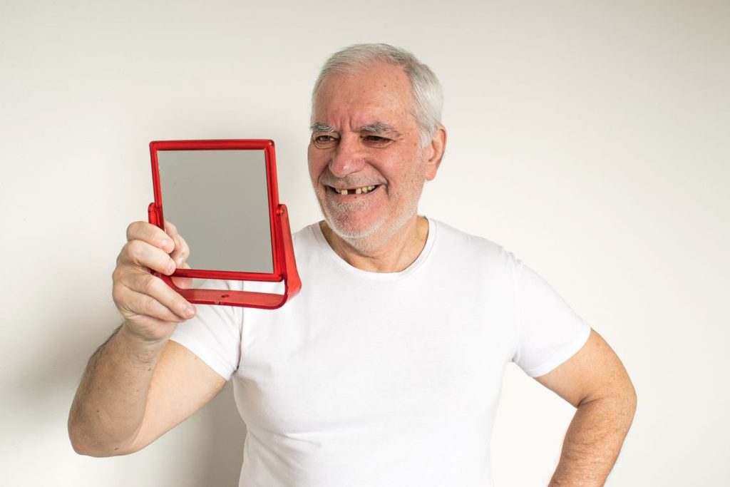 A man looking in the mirror at his smile.